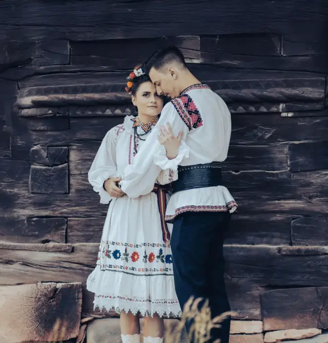 Trash the Dress-Fotoshooting im Freilichtmuseum in Cluj-Napoca mit dem Brautpaar in rustikaler rumänischer Kleidung nahe traditioneller Dorfhäuser.