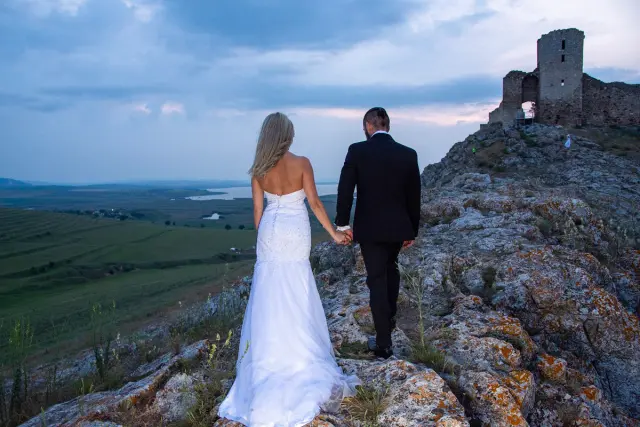 Das Brautpaar geht gemeinsam über einen malerischen Felsenhügel bei ihrer Trash the Dress-Session an den Ruinen von Enisala.